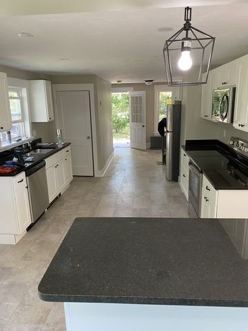 Modern kitchen with black countertops, white cabinets, central island, and a pendant light over tile flooring