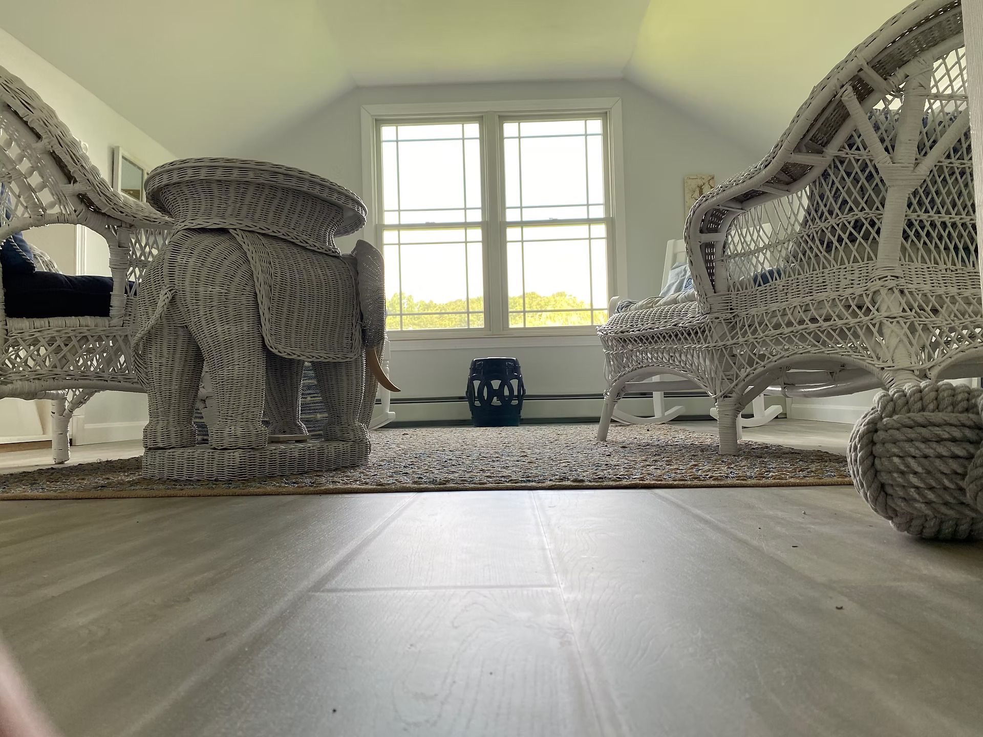 Woven chairs and a small stool in a bright room with a large window and rug