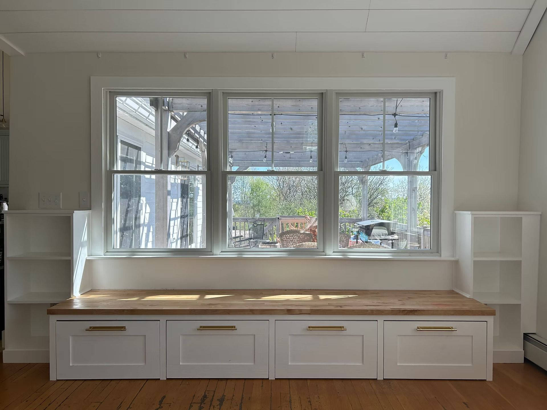 Bright window seat with white built-in bench, wooden top, and shelves in a sunroom.