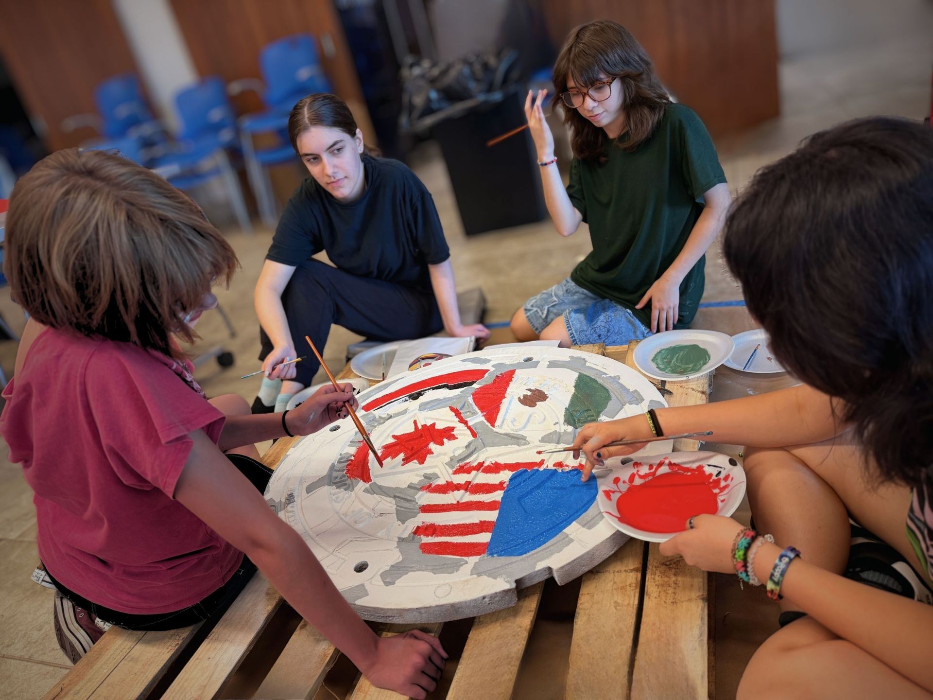 People gathered around a large painted map on the floor, working together in a studio.