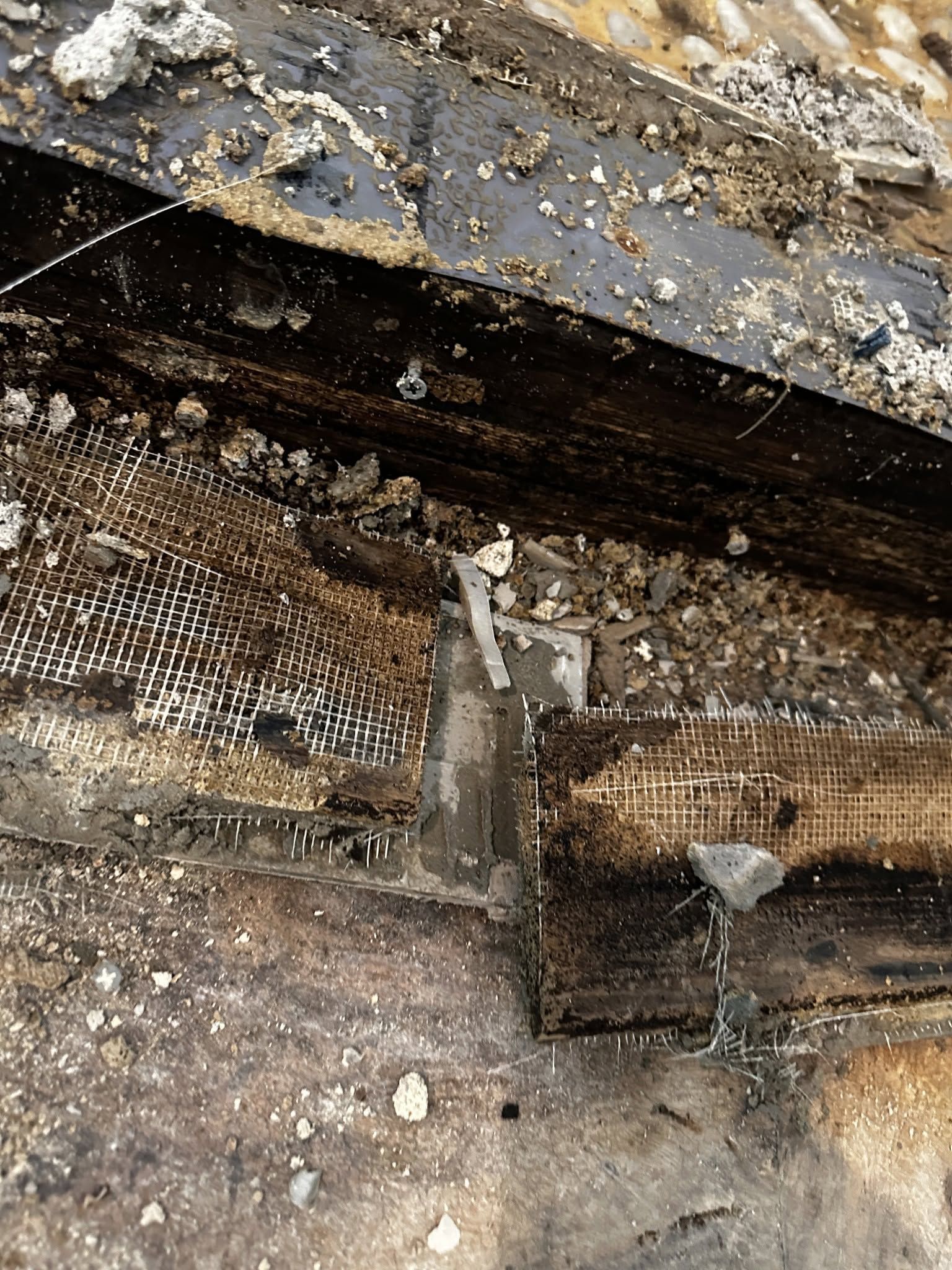 Close-up of a damaged wooden beam with peeling paint, dirt, and exposed woven material.