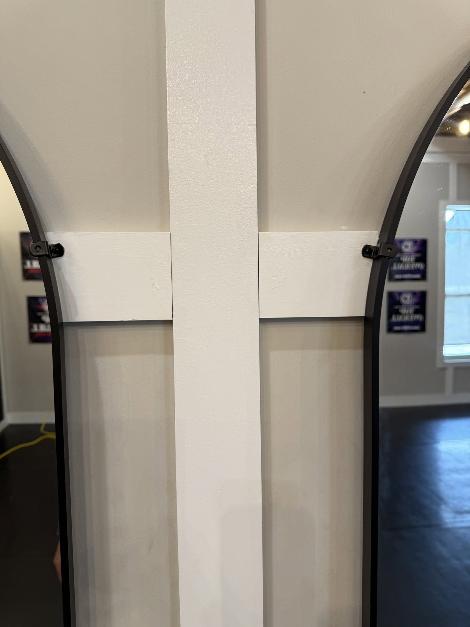 White pillar with arched wall openings in a hallway, with dark floor and small signs on the sides