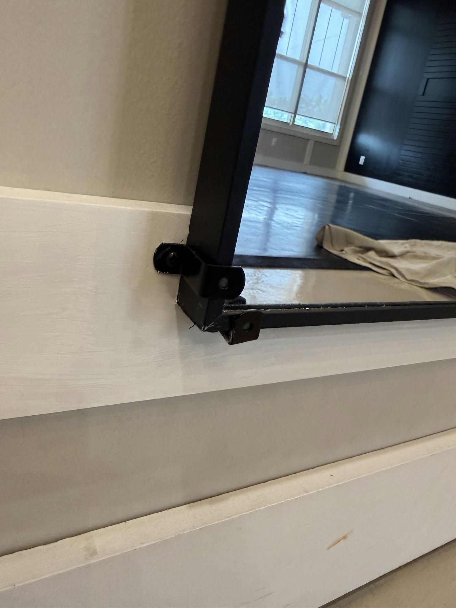 Black metal hinge on a white window or cabinet frame in a bright room.