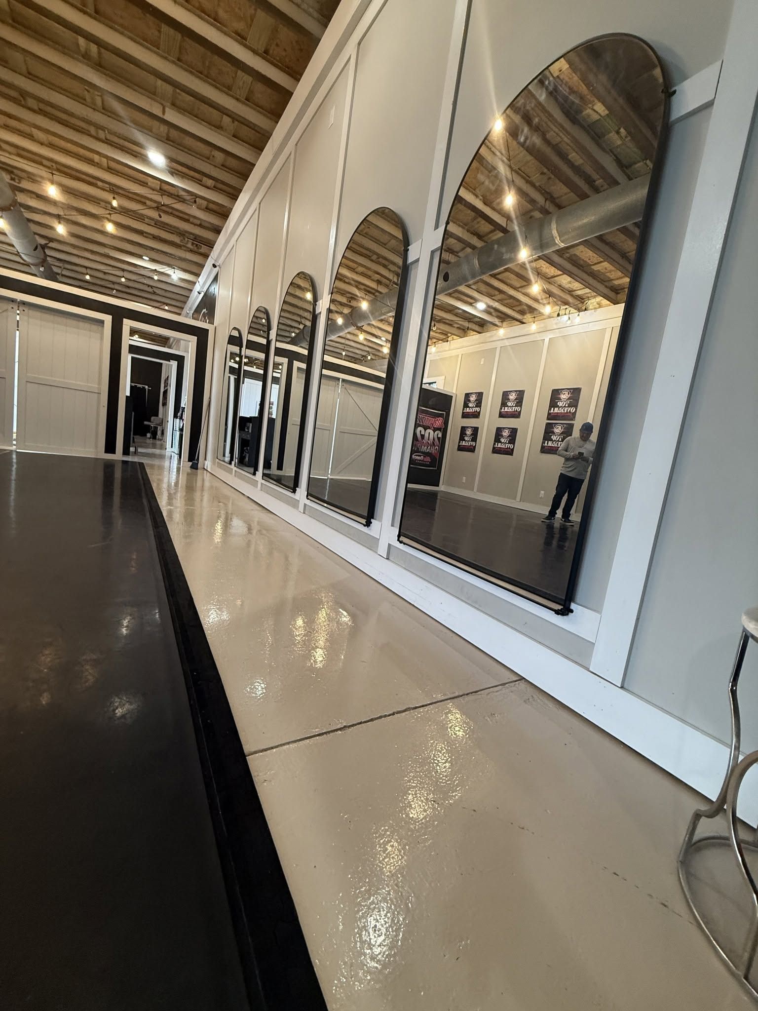 Interior hallway with arched mirrors, glossy black and cream floor, and exposed wooden ceiling beams