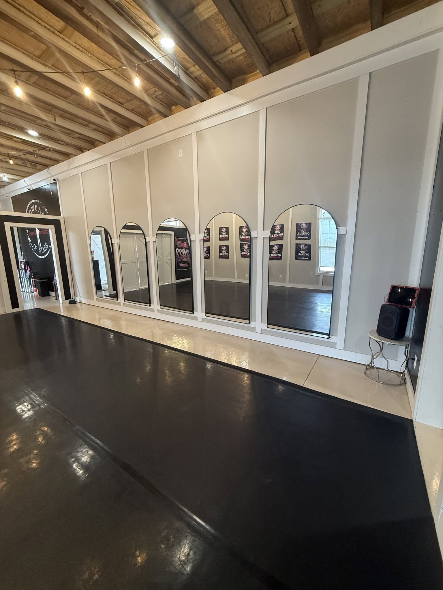 Empty dance studio with mirrored wall, white panels, and black floor under exposed wooden ceiling