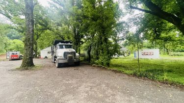 White off-road truck parked on a gravel drive under trees beside a grassy sign at a campground entrance