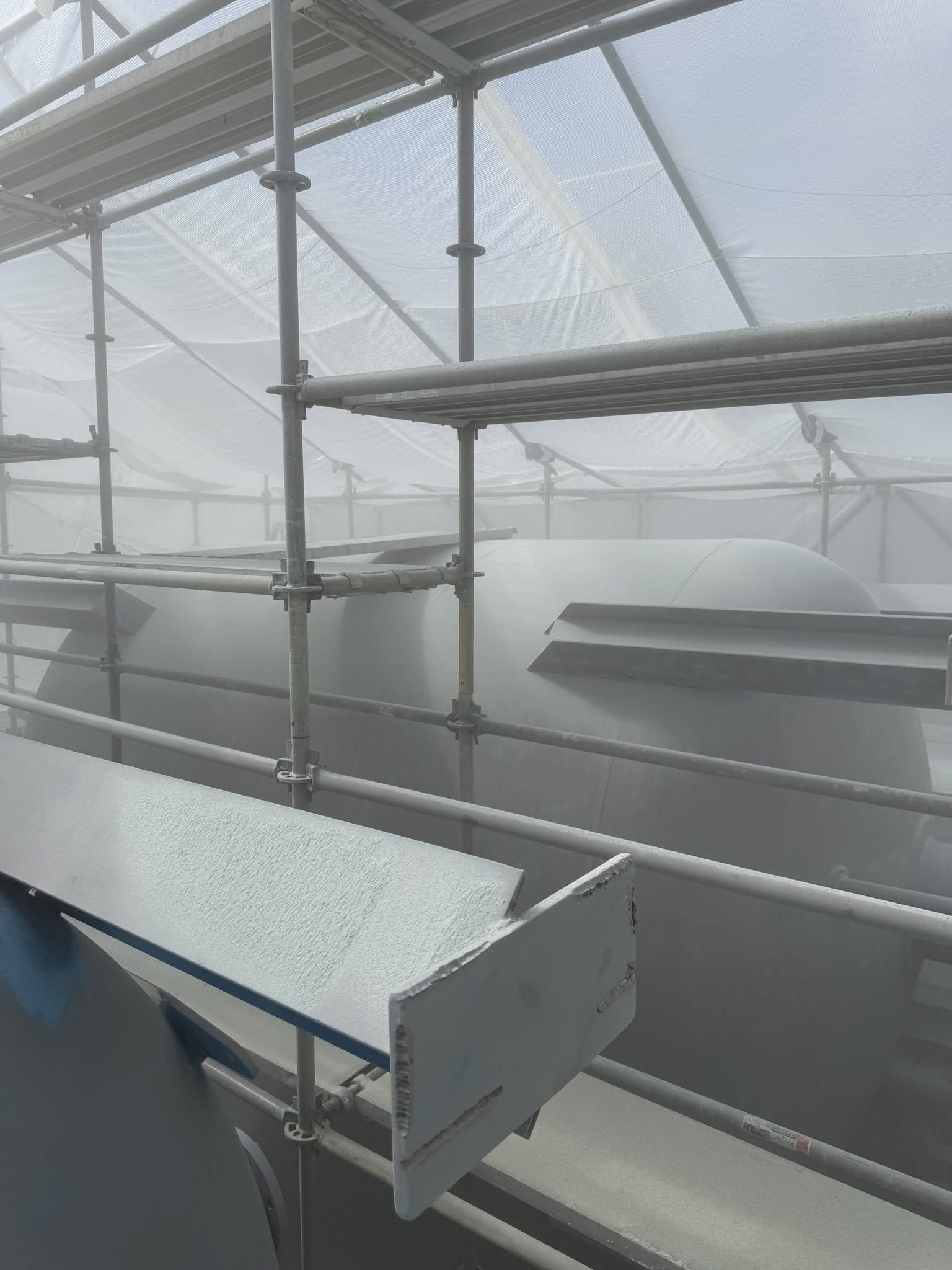 Scaffolding inside a foggy greenhouse with plastic-covered roof and metal beams