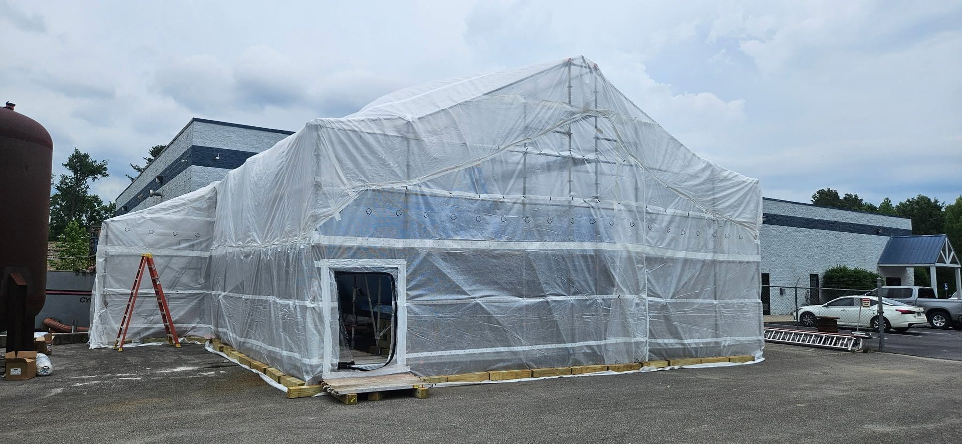 White plastic-wrapped building under construction with a ladder beside it on a cloudy day