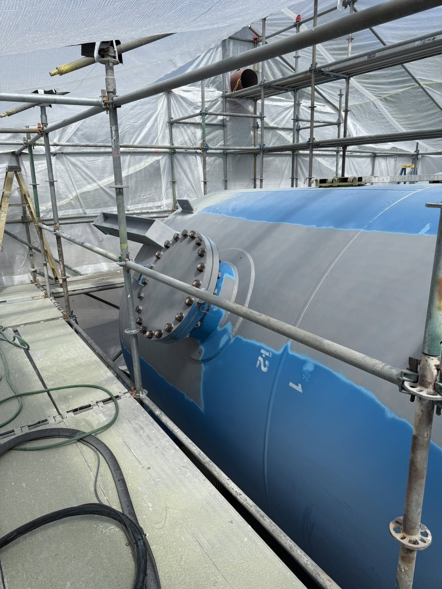 Large blue industrial tank inside a greenhouse-like structure with metal scaffolding and piping