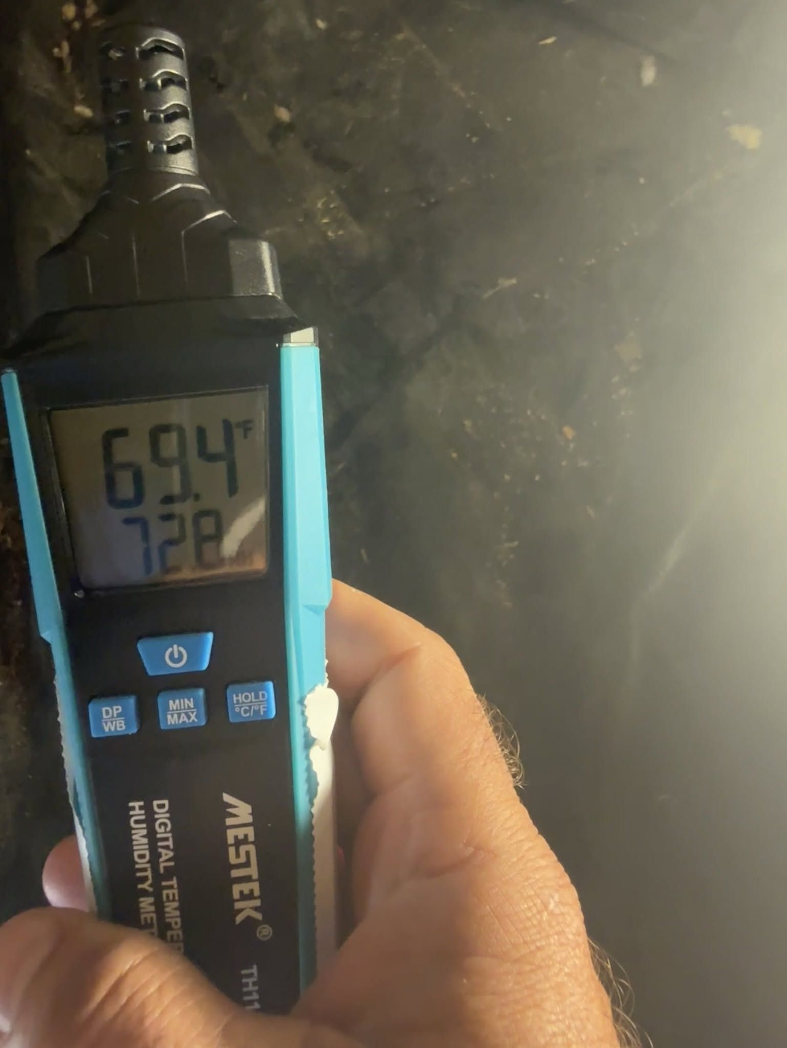Handheld blue digital meter showing 69.4 and 72.8 on its display in a dim room