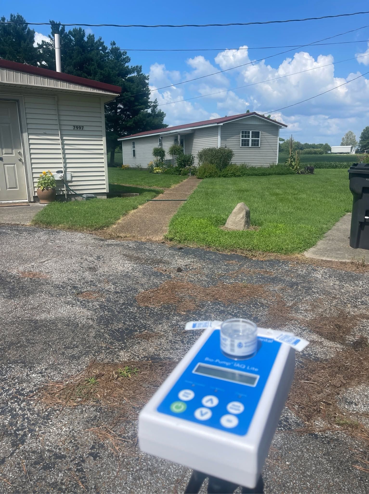 Blue-and-white handheld device in foreground, with a house, gravel driveway, and grassy yard behind it.