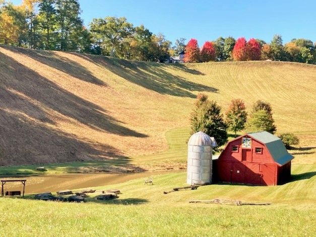 Red barn and silos in a sunny rural field with rolling hills and autumn trees
