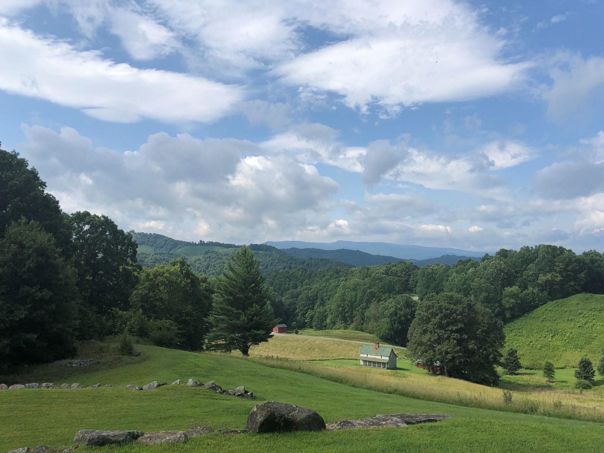 Lush green valley with rolling hills, trees, and a partly cloudy blue sky.