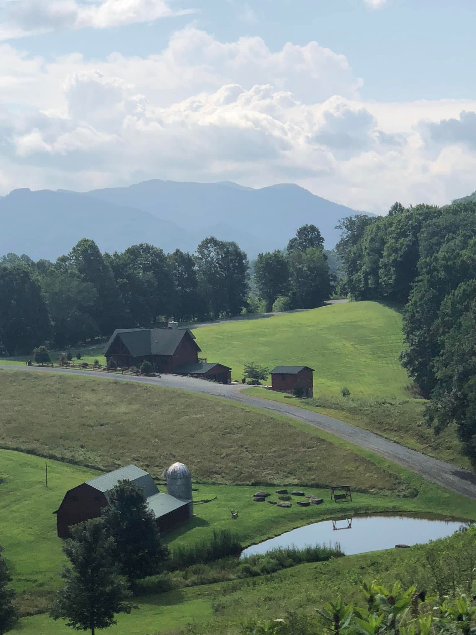 Green hills with barns, a pond, and distant mountains under a cloudy sky.