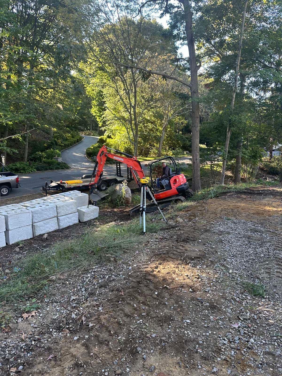 Orange excavator next to a pile of concrete blocks on a construction site in a wooded area.