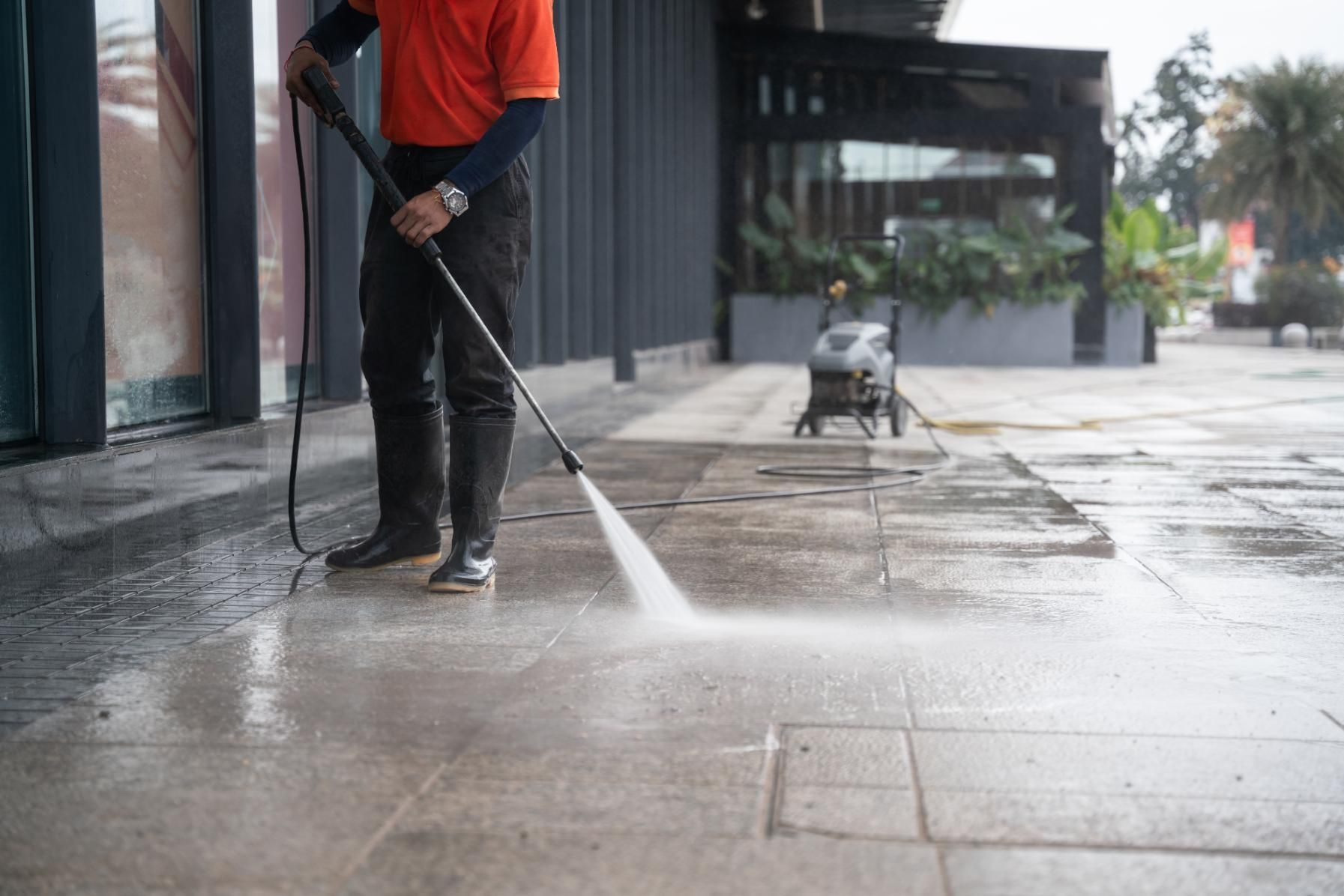 A Man is Using a High Pressure Washer to Clean a Sidewalk — Alice Springs Carpet Cleaning In Alice Springs, NT