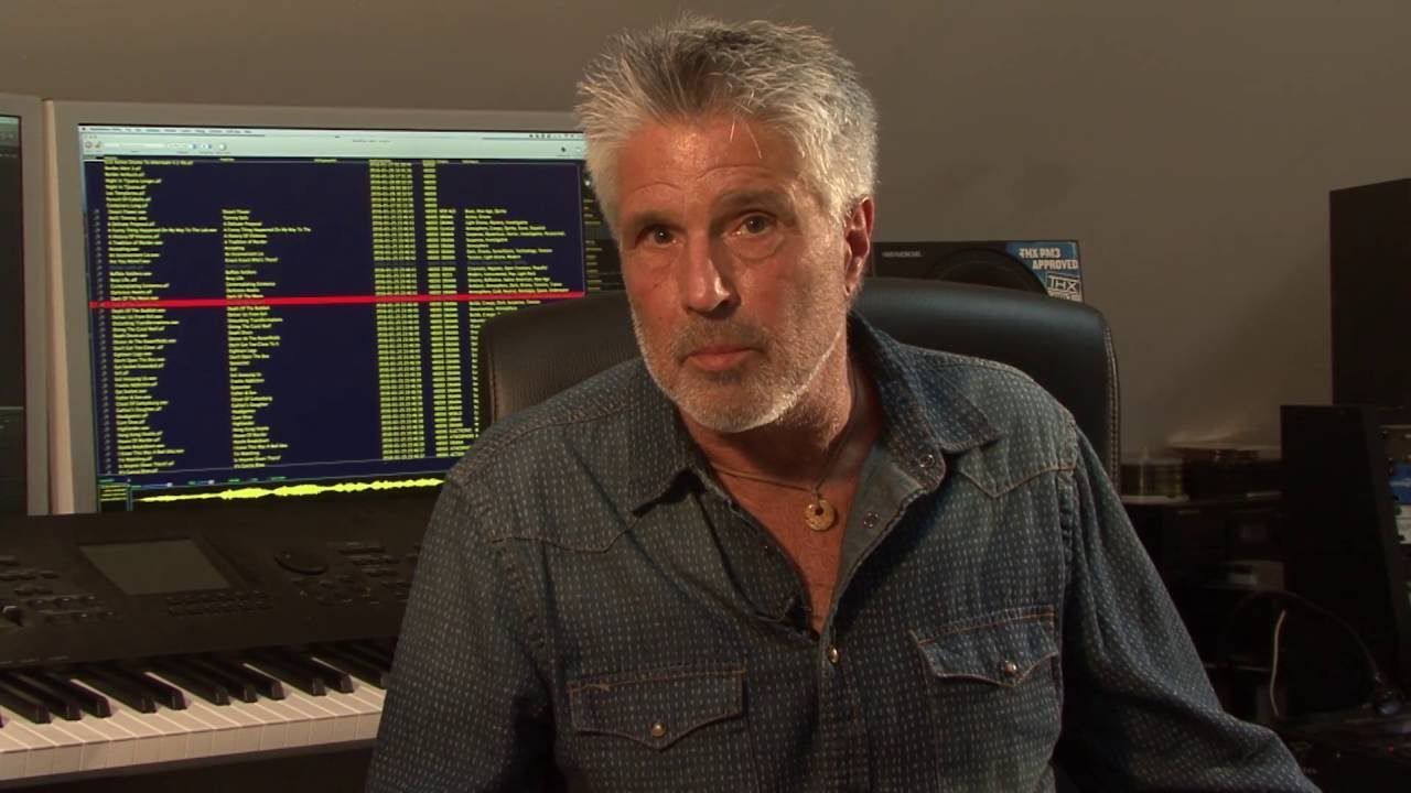 Musician Ron riddle sitting in front of a computer connected to a keyboard.