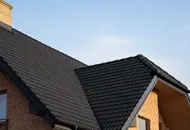 Black tile roof on a brick building with a blue sky background.