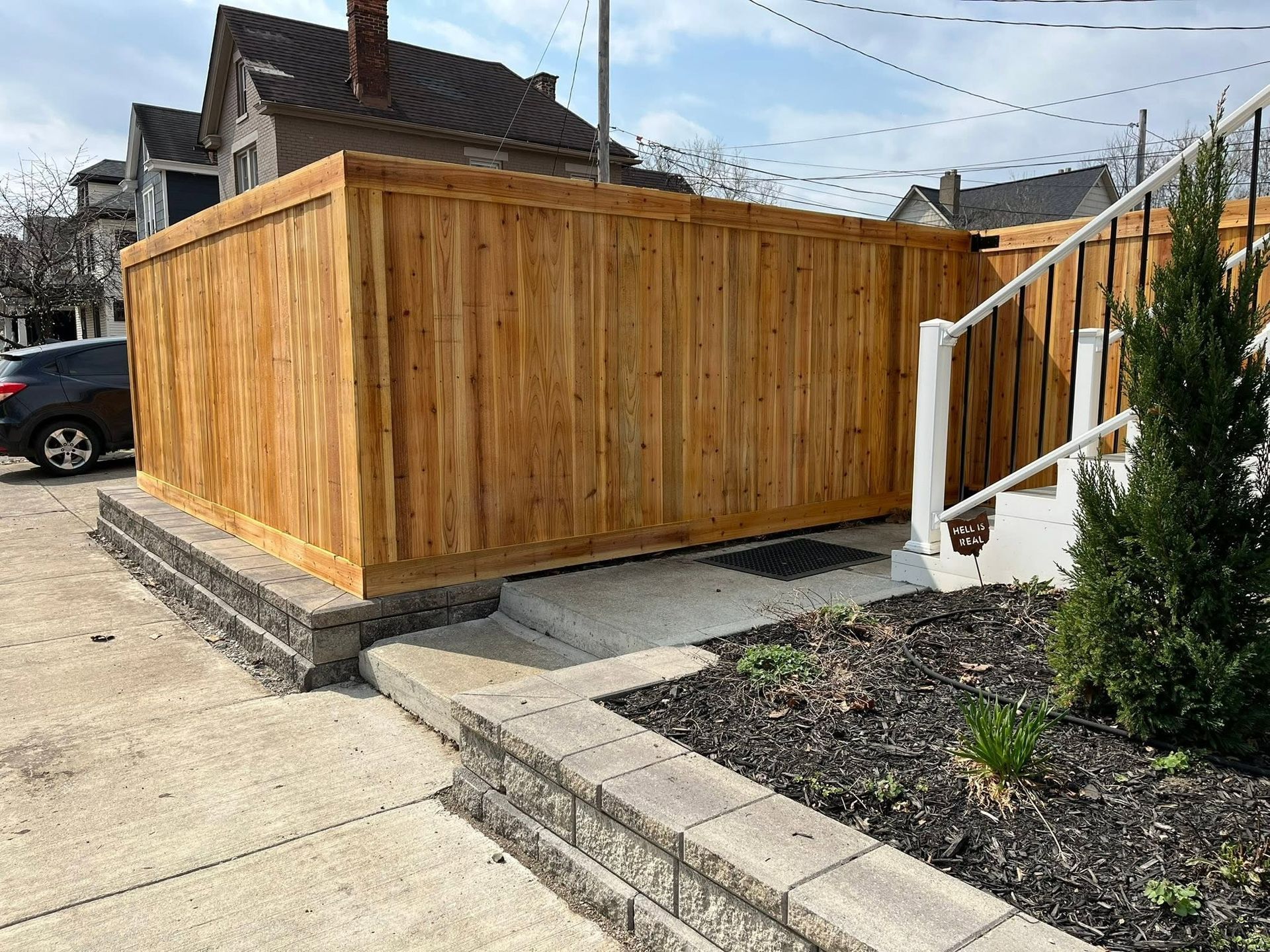 Wooden privacy fence around a utility area beside a sidewalk and concrete steps in a residential yard
