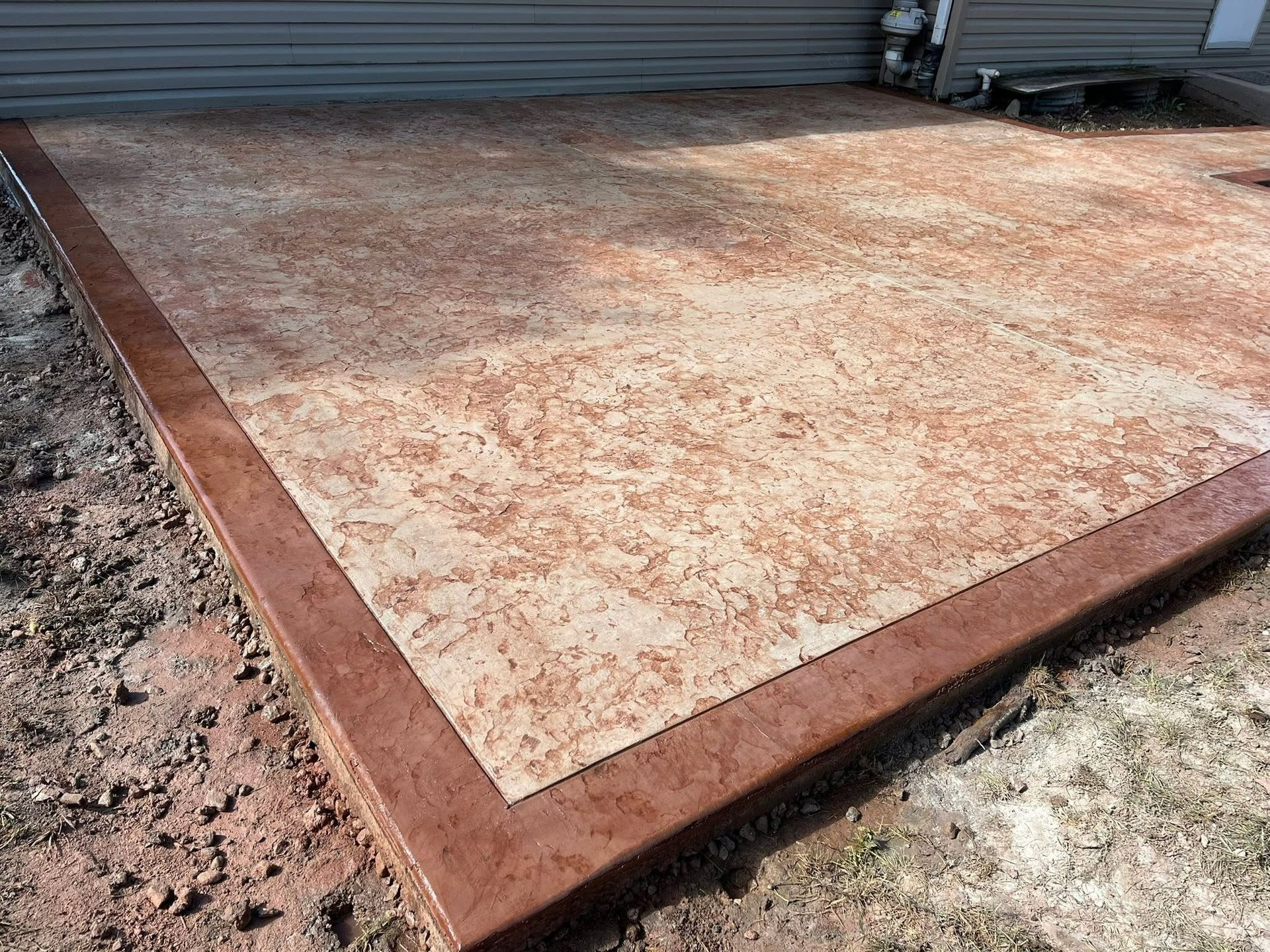 Concrete patio slab with reddish border near a metal garage door, viewed from above