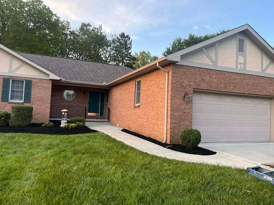 Brick suburban house with attached garage, green lawn, and a small front walkway under a blue sky