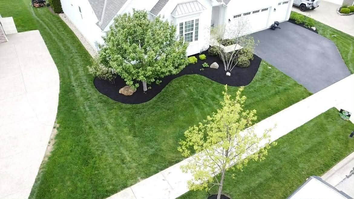 Aerial view of a suburban house with a green lawn, landscaped garden beds, and a driveway.
