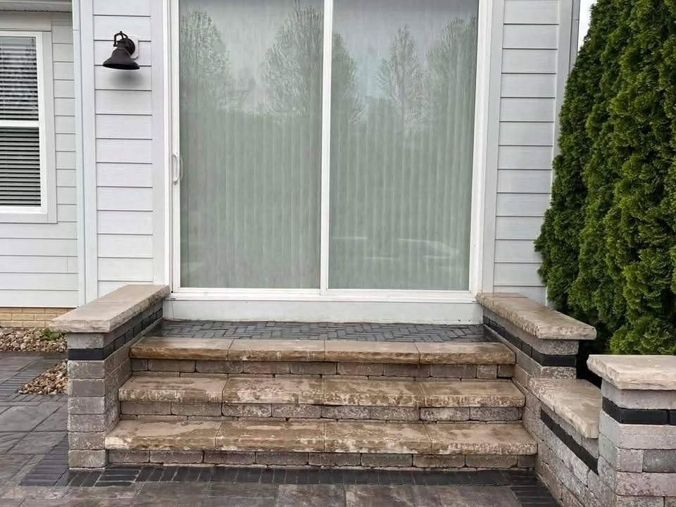Front steps leading to a sliding glass door with stone railings and white siding outdoors