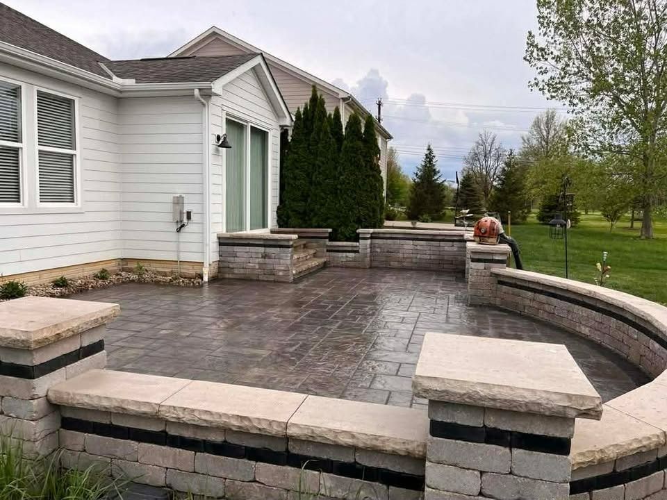 Stone patio with curved retaining walls beside a white house and green lawn