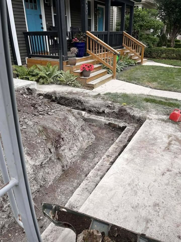 Partially demolished front walkway beside a house porch, with dirt excavation and exposed concrete edges