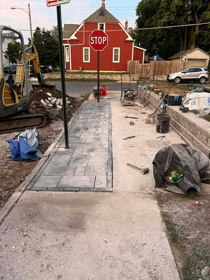 Construction crew pouring a new concrete sidewalk at a stop sign in front of a red building.