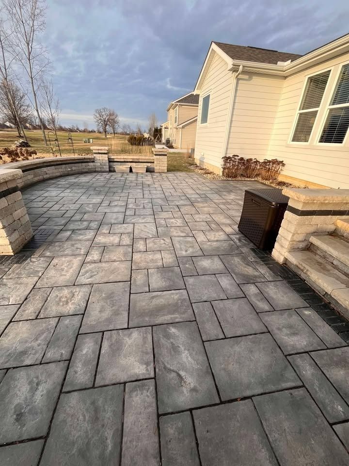 Stone patio with curved retaining walls beside a beige house under a partly cloudy sky