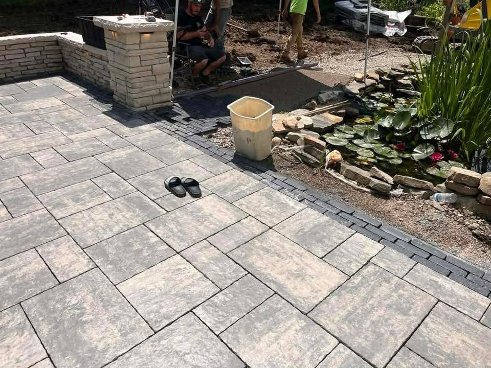 Stone patio with a small pond, garden rocks, and a pair of black sandals near a brick planter.