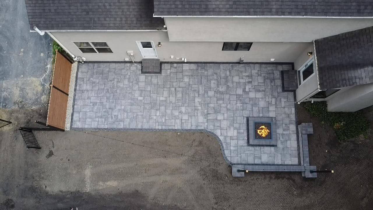 Overhead view of a house patio with gray pavers and a small fire pit beside the wall