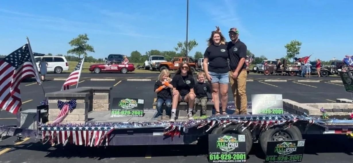 Family posing on a decorated truck float with American flags in a parking lot under a blue sky