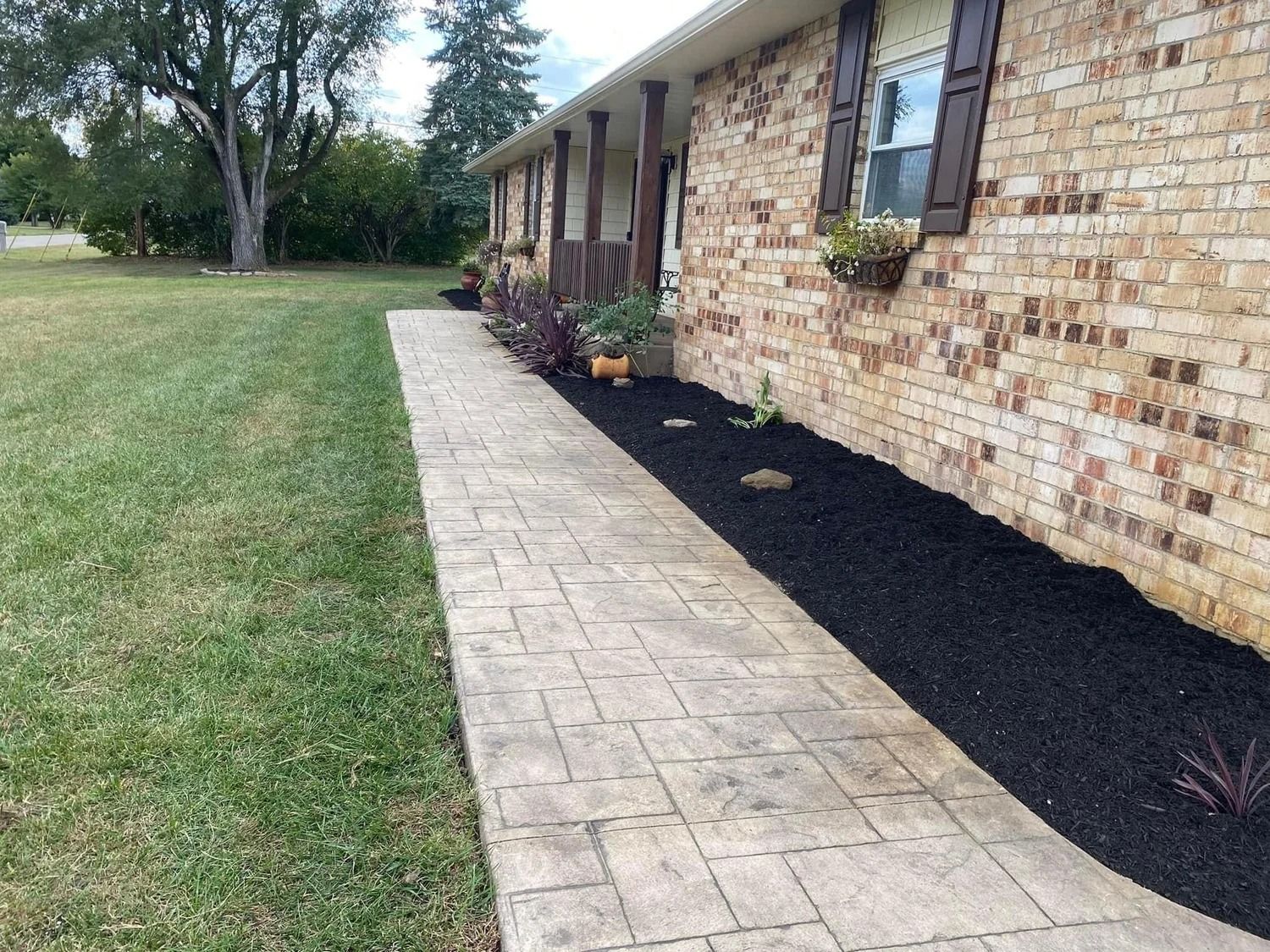 Brick house with a paved walkway, black mulch beds, and a grassy yard.