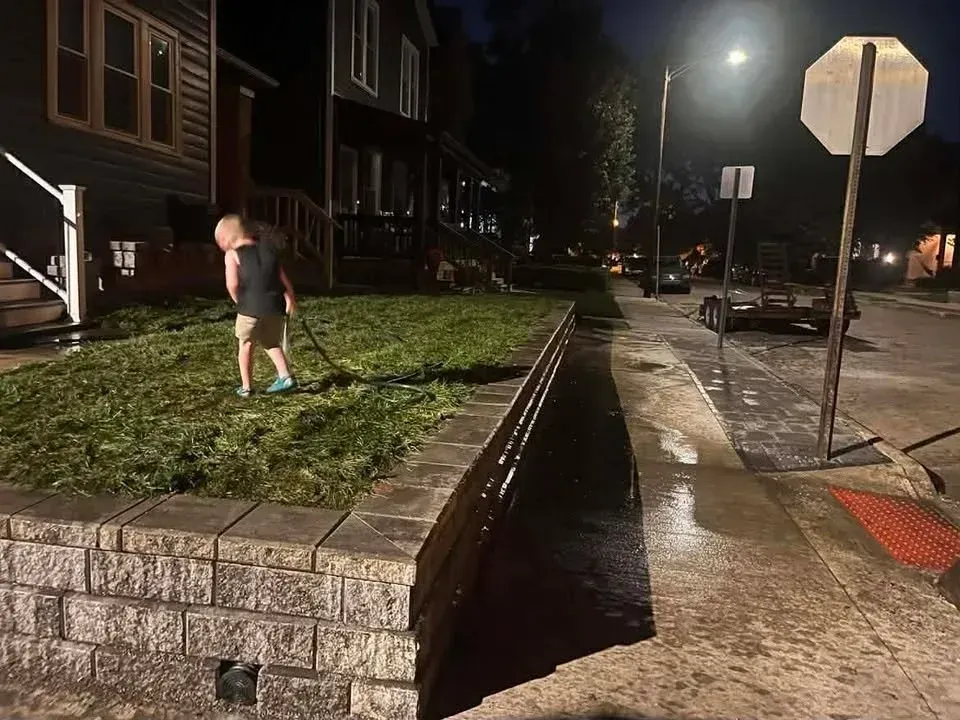 Person walking on a grassy sidewalk beside a brick retaining wall at night on a residential street