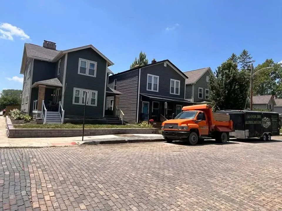 Dark houses on a residential street with an orange truck and trailer parked by the curb