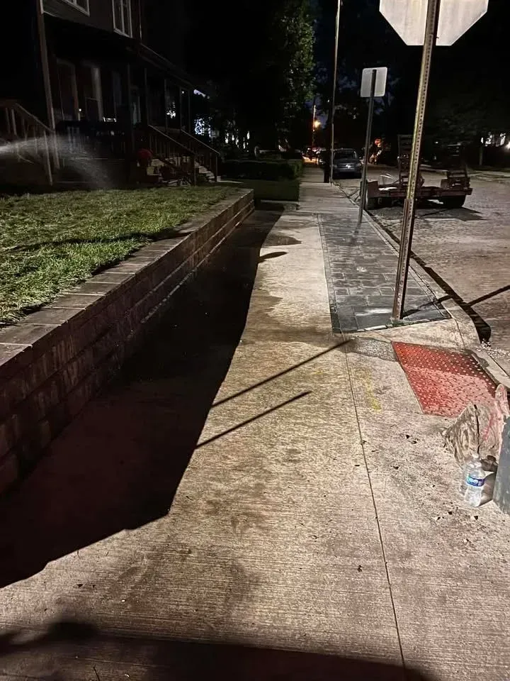 Nighttime sidewalk with a raised brick planter, street signs, and a parked car in the distance