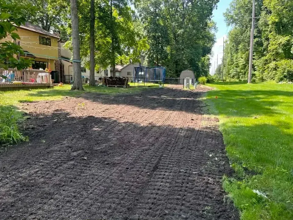 Freshly graded dirt path beside a green lawn and trees in a suburban yard