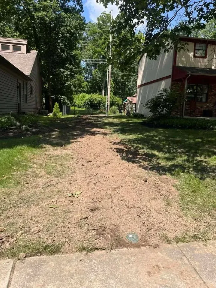 A dirt path between two houses leads to a green, tree-lined yard.