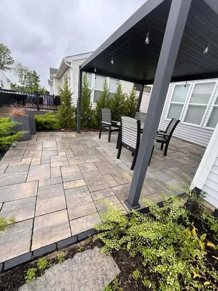 Backyard patio with stone pavers, black pergola, outdoor dining table, and white house siding