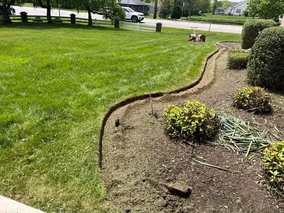 Curved garden bed edging between green lawn and mulch, with shrubs and a sidewalk nearby.