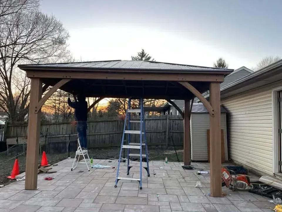 Backyard patio with a wooden pergola, ladders, and orange cones during construction