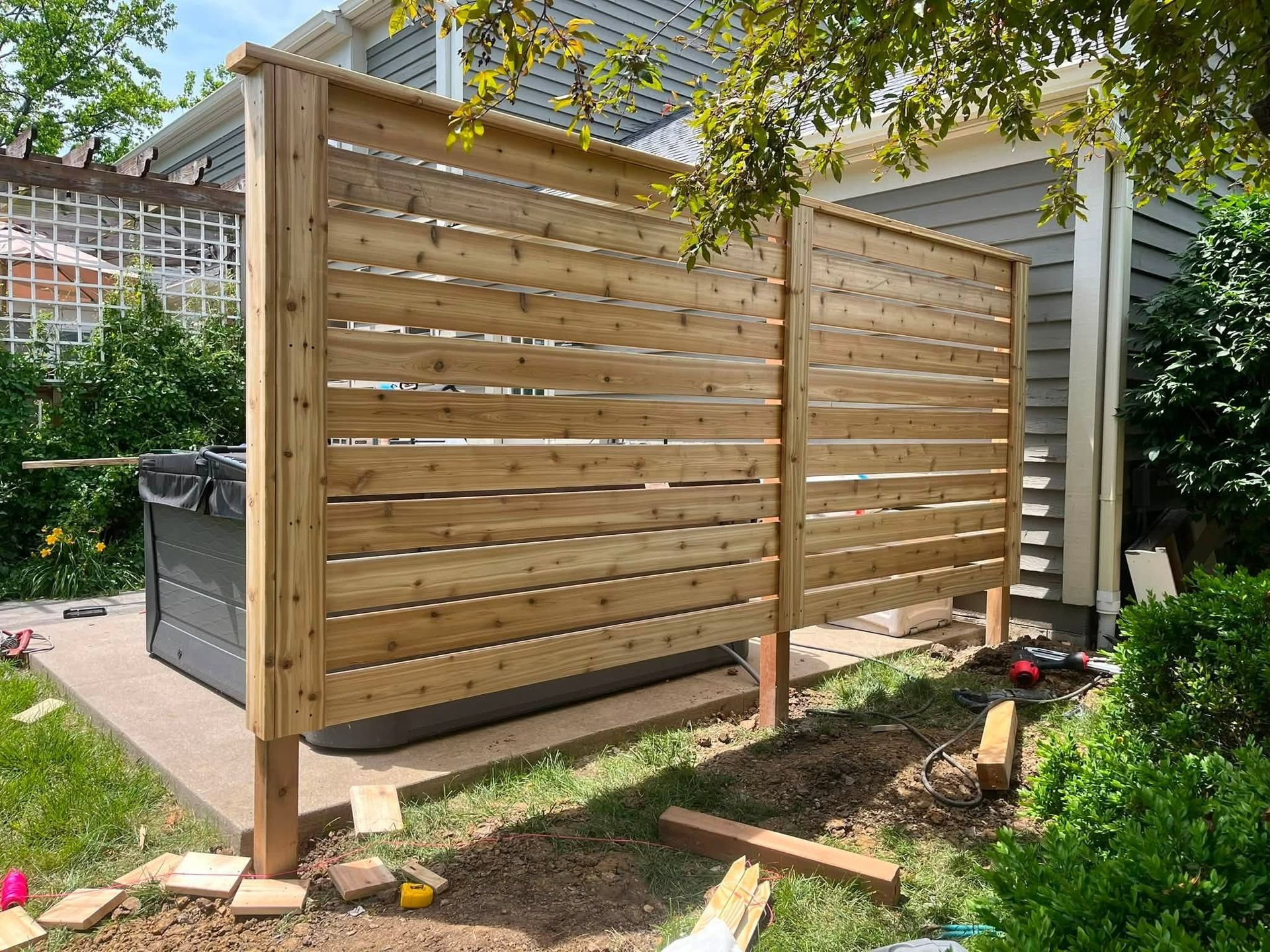 Wooden slat privacy fence beside a house, with tools and boards on the ground during installation.