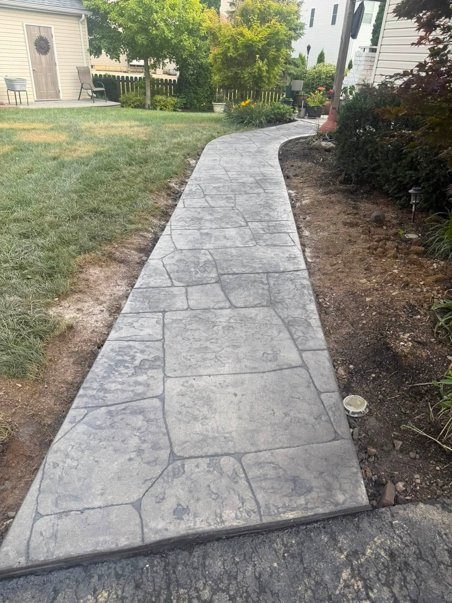 Curved stamped-concrete walkway leading through a landscaped yard to a house entrance