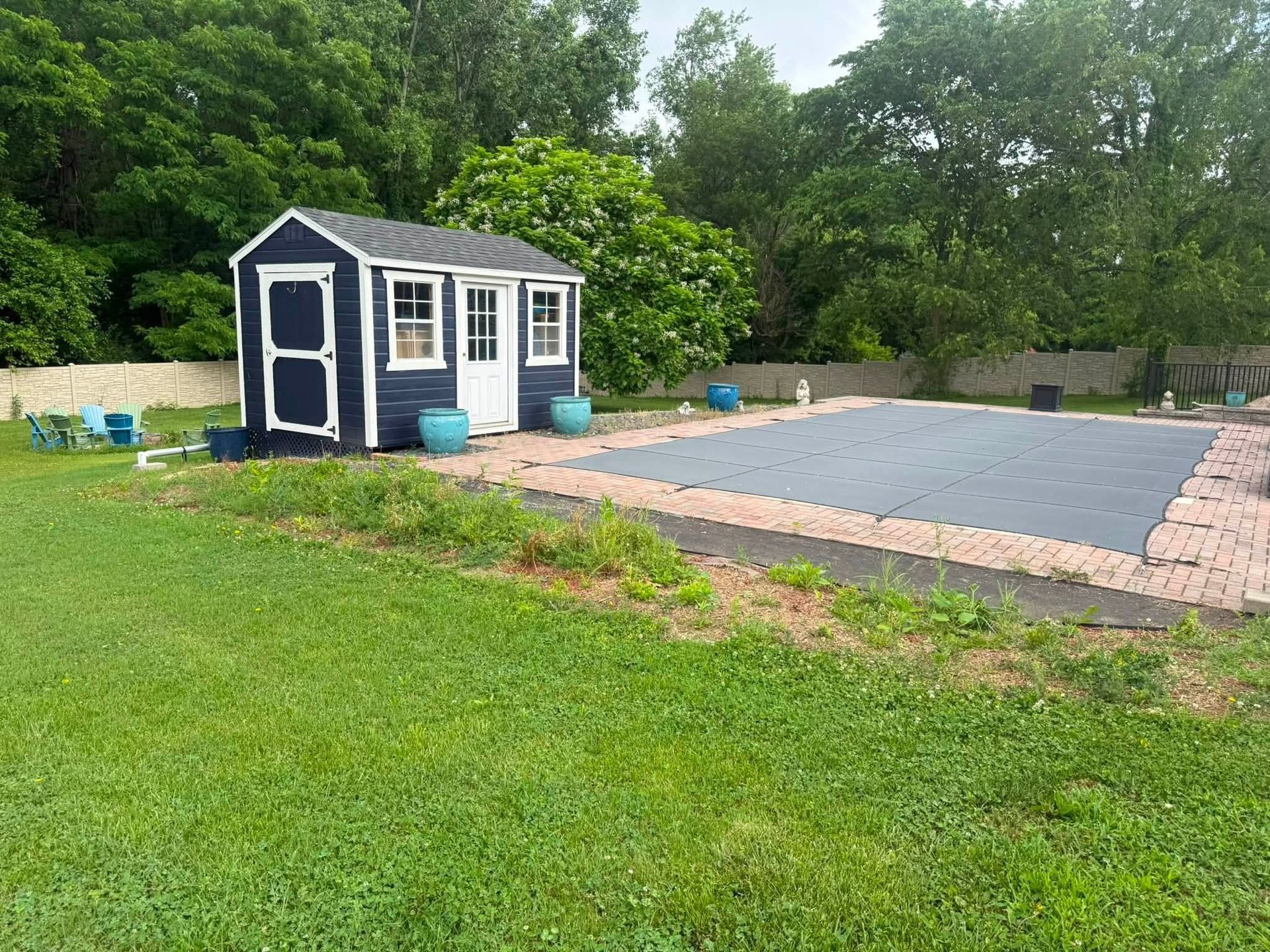 Backyard with a blue shed and a covered rectangular pool surrounded by pavers