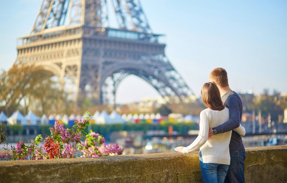 A man and a woman are standing in front of the eiffel tower in paris.