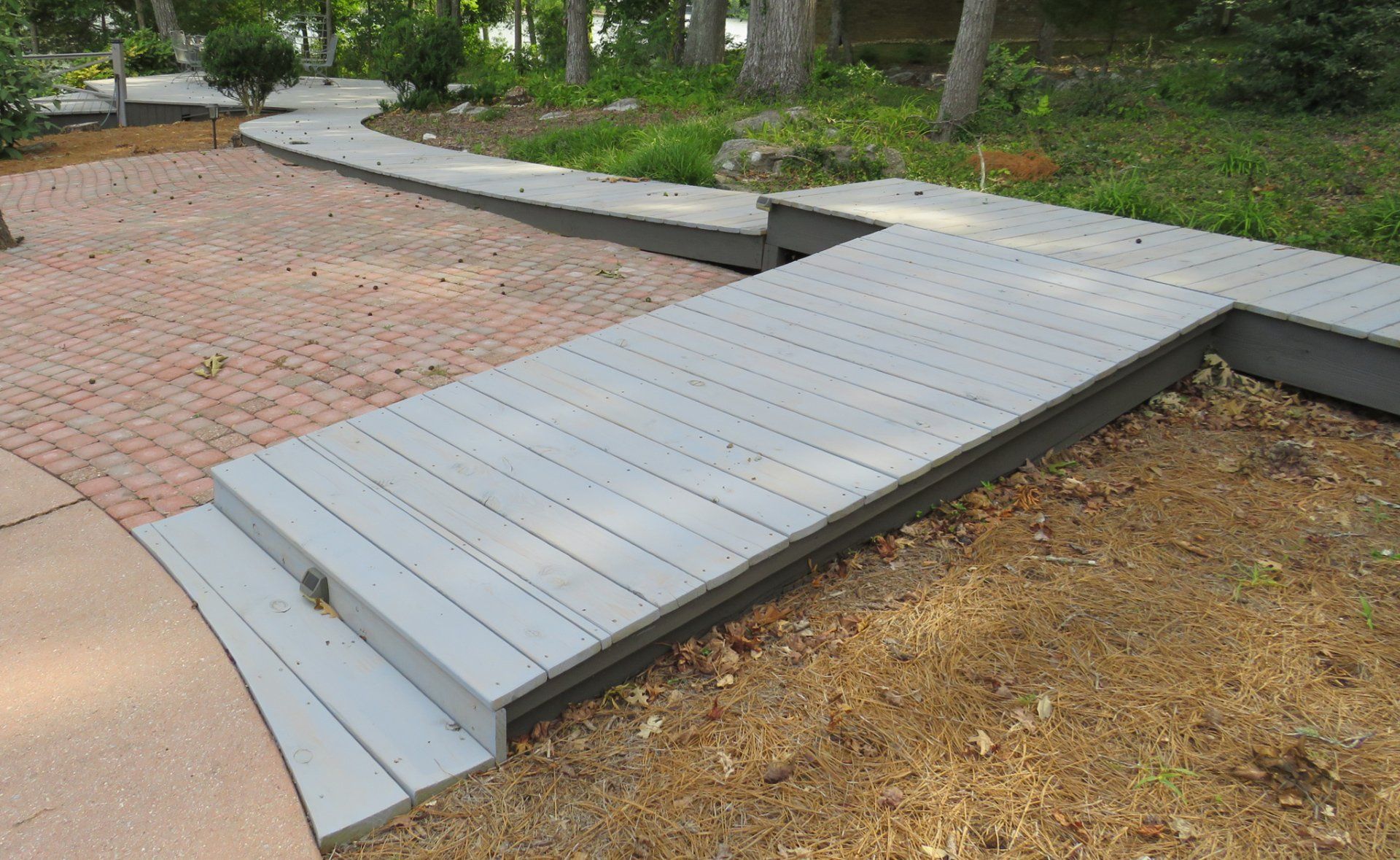 A wooden walkway with steps leading to a brick walkway.