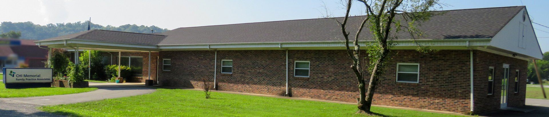 A brick house with a brown roof is surrounded by grass and trees.