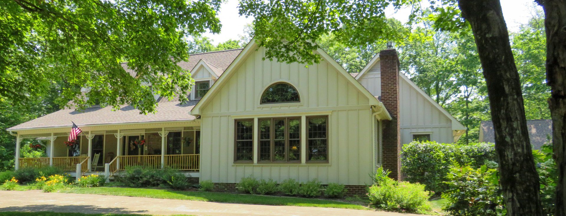 A white house with a screened in porch is surrounded by trees.